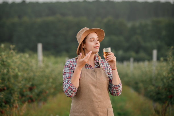 秋收时节，站在果园花园里的女农民，面带微笑，吸着盛在玻璃杯里的可口苹果汁的香气。收获的时间图片下载
