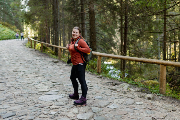 时尚的女游客徒步在秋天的森林步道。快乐的红头发的人在积极徒步旅行的衣服上走在自然背景。旅行和积极的生活方式概念。全身照片。图片下载