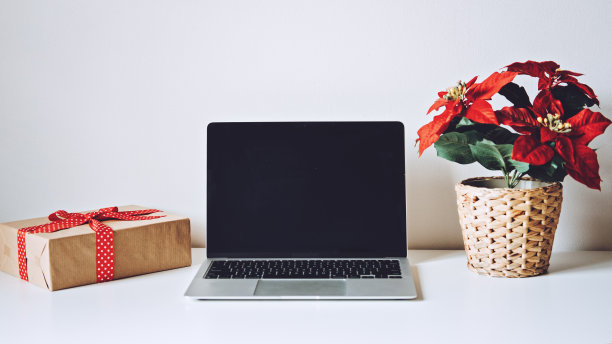成功的圣诞季电子商务，圣诞网上购物。打开笔记本电脑显示屏幕，一品红圣诞花和礼盒在白色的桌子上图片下载