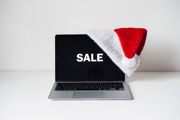 显示屏笔记本电脑与文字销售和圣诞老人帽子在白色的桌子上。节日家庭办公室办公桌工作区。圣诞网购，冬季促销，圣诞电商图片下载