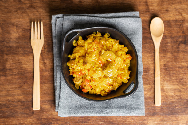 黑色质朴的盘子上有一份肉海鲜饭，在木制背景上，俯视图。图片下载