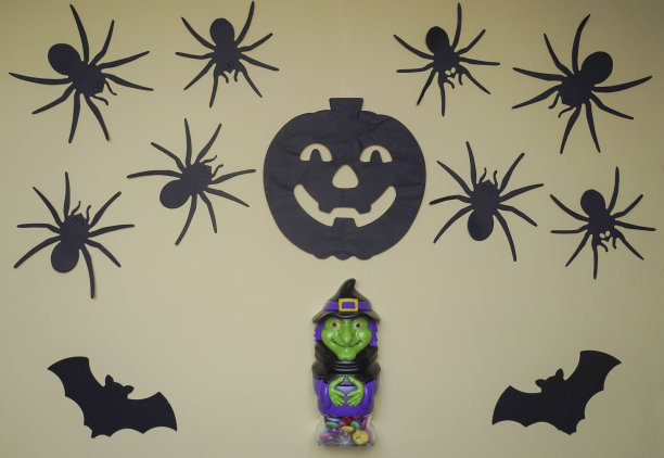 恐怖的万圣节女巫站在一个灯光背景的特写，后面挂着可怕的黑南瓜，蜘蛛和蝙蝠。可爱的角色在怪物服装。万圣节的概念。节日装饰玩具图片下载
