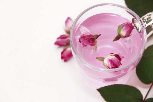 粉红色的茶装在透明的玻璃杯里，白色背景上有粉红色的玫瑰花蕾图片下载