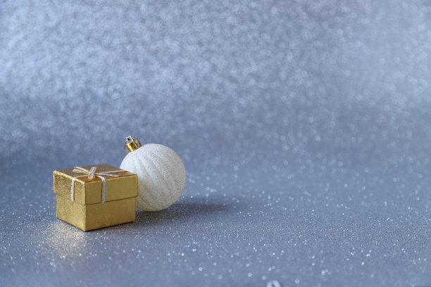 金色的礼品盒和白色的圣诞球装饰在银色闪闪发光的背景。选择性对焦照片图片下载