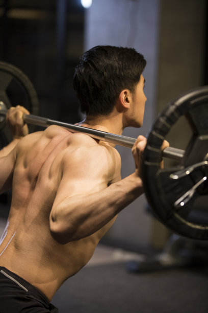 年轻男子举杠铃进行重量训练，背部肌肉特写图片下载