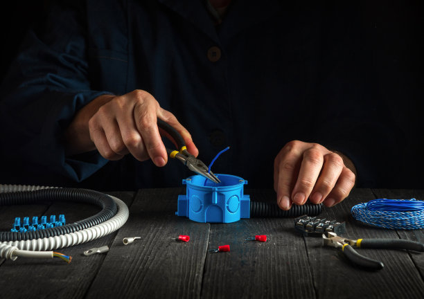 一位电工师傅工作时的手特写。安装电缆或电线到蓝色接线盒。电气设备的安装和维修的想法。图片下载