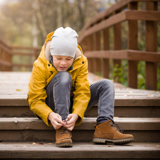 在一个寒冷的秋日，可爱的孩子系着鞋带在城市公园散步。男孩在户外图片下载