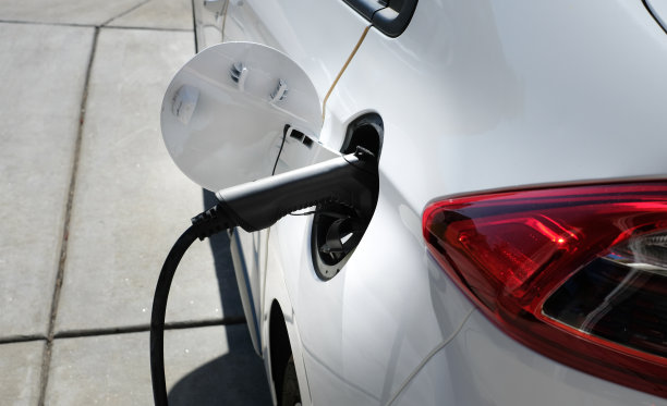 白色的电动汽车带着充电器和插座在车道上充电。家庭充电站的环保交通和未来的概念。俯视图图片下载