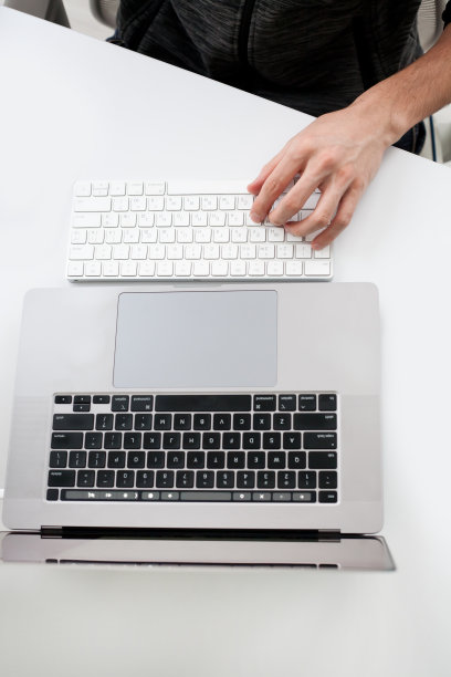 男子在工作场所用笔记本电脑在白色表面打字的剪裁镜头图片下载