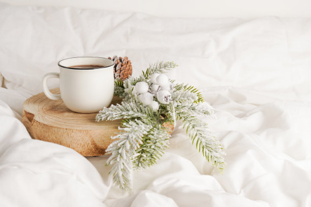 咖啡杯放在木头上，白色的床上有圣诞装饰。在床上吃早餐。冬天的早晨图片下载