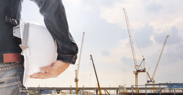 身穿牛仔裤、头戴白色头盔的工程师在大型工程中用起重机监督施工。图片下载