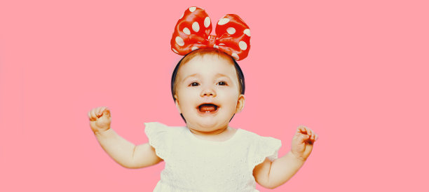 欢快的笑婴儿的肖像与蝴蝶结在头部孤立的粉红色背景图片下载