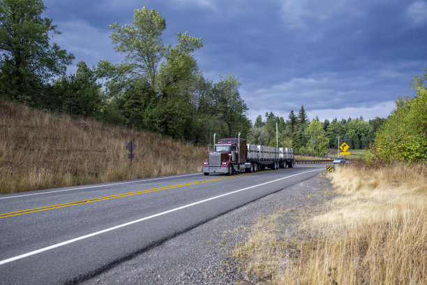 勃艮第大卡车经典半挂车运输货物的箱子固定在平床半挂车运行在蜿蜒的道路上与山的两侧图片下载