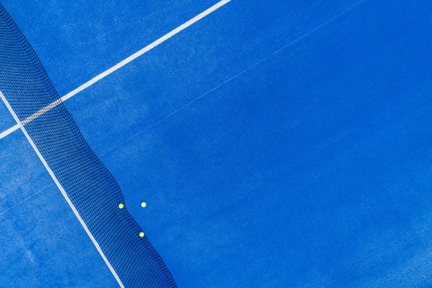 无人机鸟瞰图的三个球接近网在一个蓝色的桨网球场图片下载