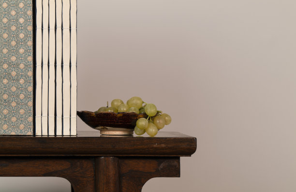 白墙上的木桌上摆放着中国古董盘上的白葡萄和中国传统书籍图片下载