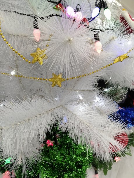 白色圣诞树背景。白色圣诞装饰与金色星星和灯在冷杉树枝。垂直的。白色圣诞壁纸图片下载