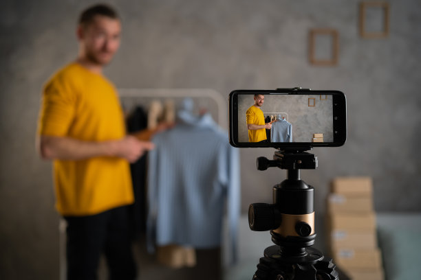 一名男子博主在他的商店录制视频和直播时，在智能手机摄像头前展示衣服。在网上直播图片下载
