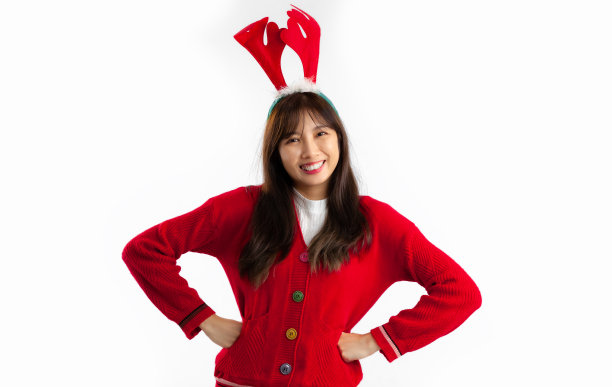亚洲妇女在红色毛衣戴驯鹿角头带站着摆姿势看相机白色背景。图片下载