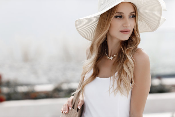 一个漂亮的年轻女人，金发碧眼，戴着一顶夏天的大边白帽子，独自一人在户外穿着白色的夏天连衣裙。图片下载
