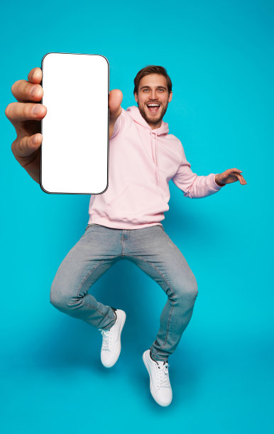 英俊兴奋的男子指着空的智能手机屏幕在浅蓝色背景上摆姿势，对着相机微笑图片下载