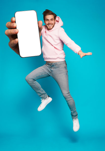 英俊兴奋的男子指着空的智能手机屏幕在浅蓝色背景上摆姿势，对着相机微笑图片下载