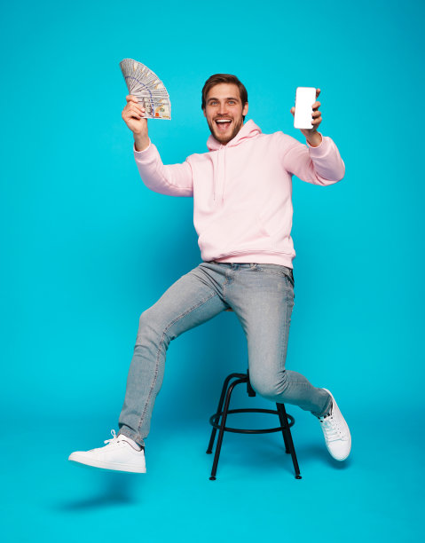 兴奋的家伙拿着空白的智能手机和美元现金，男人坐在椅子上庆祝经济成功图片下载