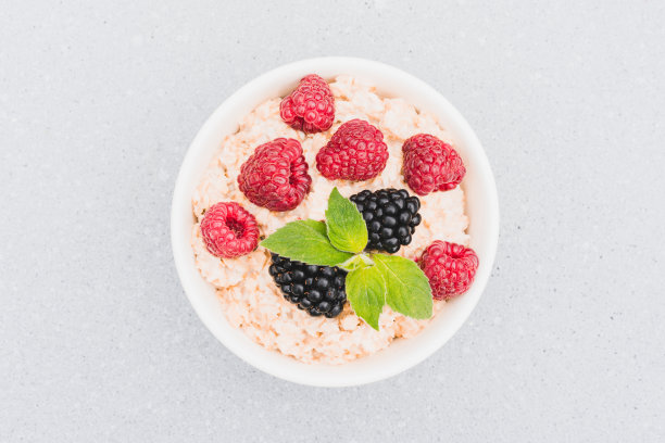 燕麦粥配上浆果和薄荷叶放在桌上的白碗里。早晨超级食物粥食谱。健康早餐的建议。以上观点图片下载