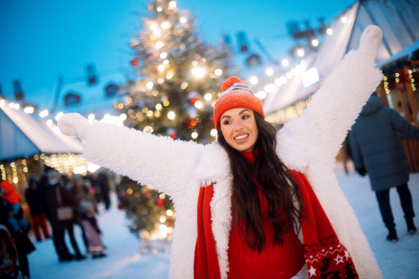 迷人的年轻女子在圣诞市场旁边的新年树。图片下载