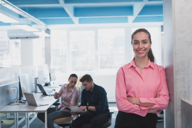 年轻微笑的商业女性在创意开放空间联合办公的初创公司办公室的肖像。成功的女商人站在办公室与文案空间。同事在后台工作。图片下载