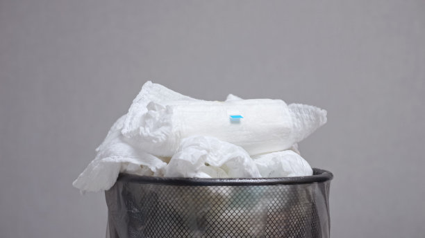 有人把用过的纸尿裤扔进装有纸尿裤的箱子里，箱子靠在灰色的墙上图片下载