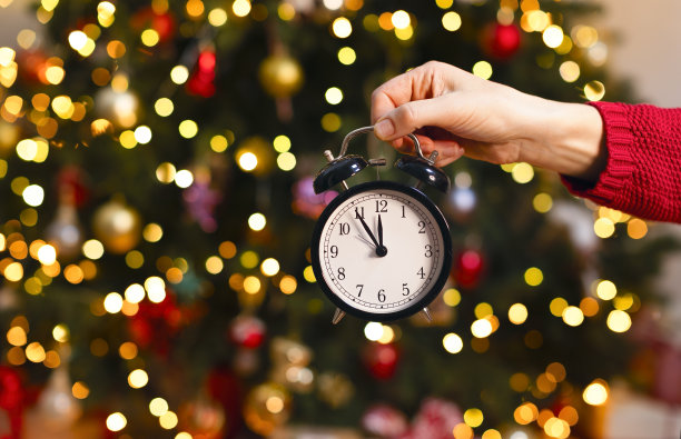 这是一张圣诞照片，有空间复制，手拿着时钟，背景是一棵云杉树。图片下载