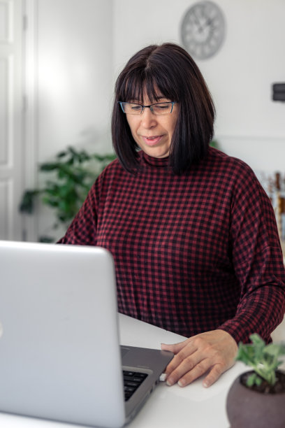 有魅力的中年女性坐在桌子旁，用笔记本电脑工作。图片下载