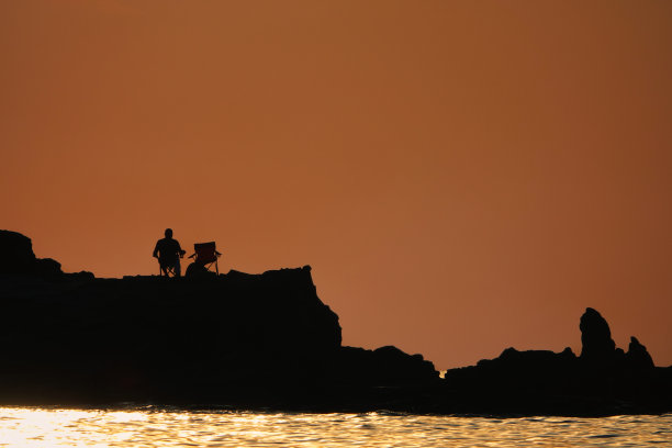 一个孤独的人坐在日落的悬崖上，欣赏着全家人的夜景图片下载