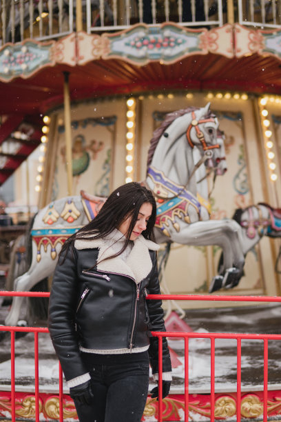 美丽的白人妇女穿着温暖舒适的衣服走在圣诞集市上，雪花落在节日灯光的背景上。图片下载