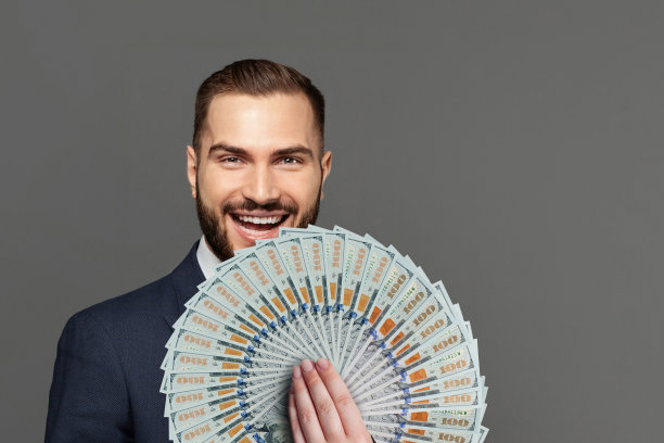 快乐的成功商人的肖像与钱风扇在灰色的工作室墙壁背景图片下载