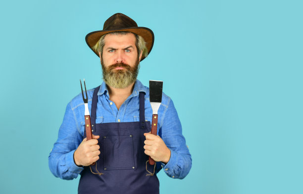 烹饪牛排。烹饪用具。夏季野餐。烧烤是美国传统。烹饪概念。中罕见的。烧烤食物。工具烤肉。穿着围裙的男人拿着烧烤架。农民推广烧烤设备图片下载