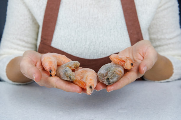 一个穿着棕色围裙的女孩手里拿着冷冻的虎虾和国王虾放在桌子上。冰釉制品图片下载