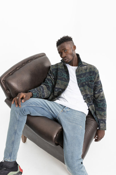 一个非洲裔美国人坐在白色背景的皮革扶手椅上。穿着冬季衬衫，白色t恤和蓝色牛仔裤的酷黑魅力男子。图片下载
