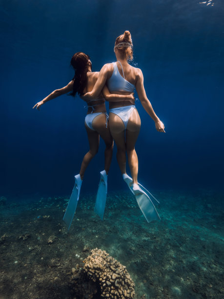 在深蓝色海洋中拥抱和滑行的两名穿着时尚的自由潜水女孩图片下载