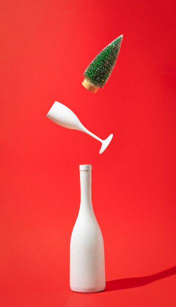 红色背景的白酒瓶、葡萄酒杯和圣诞树。最小派对概念。新年和圣诞节庆祝的想法。图片下载