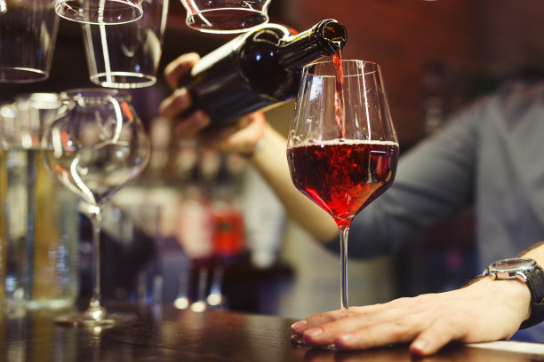 特写镜头，半暗的酒吧里，酒保把红酒倒进柜台的玻璃杯里图片下载