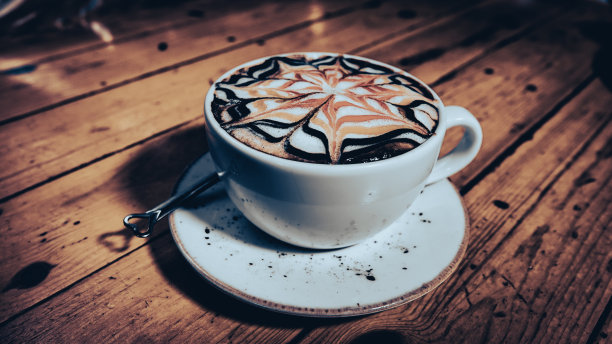 复古的棕色桌子上放着一杯漂亮的拉花图案的拿铁咖啡。图片下载