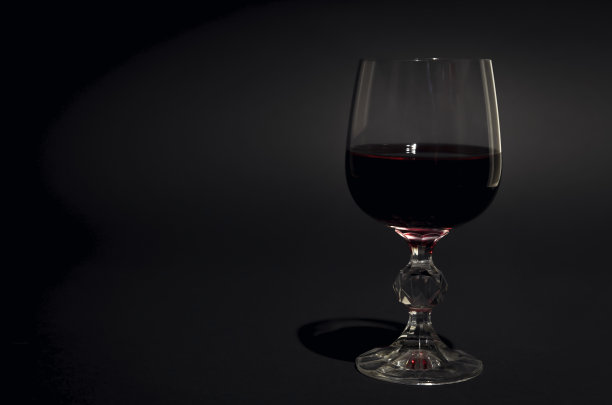 一杯红酒。红酒装在透明的玻璃杯里。黑色背景。专注于玻璃。图片下载