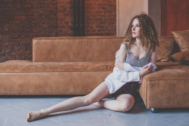 漂亮的女人在白色衬衫卷发坐在棕色沙发附近图片下载