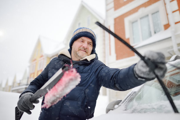 成年男子在降雪后用刷子清洁汽车。暴风雪后汽车引擎盖上的雪堆。暴风雪后城市道路交通困难。冬天的天气。图片下载