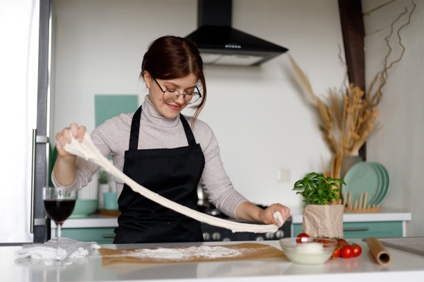 最大的爱好是做披萨。快乐的年轻女子在厨房里拉伸面团。图片下载