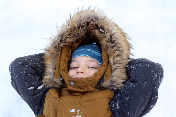 一个英俊的男孩躺在雪地上，双臂交叉放在脑后。他看着镜头，微笑着。图片下载