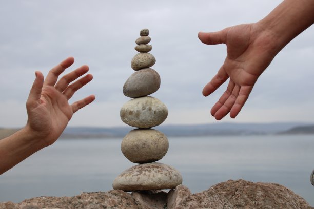 一只手在鹅卵石上建立平衡。海边鹅卵石堆得完美平衡。平衡、和谐和冥想的概念。帮助或支持某人成长或晋升的。图片下载