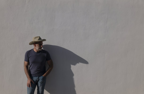 成年男子的肖像在牛仔帽对着白色的墙与阳光和阴影图片下载