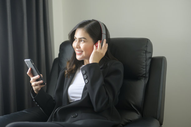 年轻放松的商业女性使用智能手机，在现代办公室听音乐。图片下载